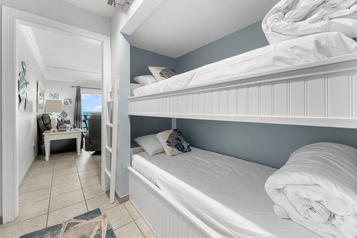The Summit 1130 – Bunk room with two beds, ladder, and view of living area and blue sky through window.