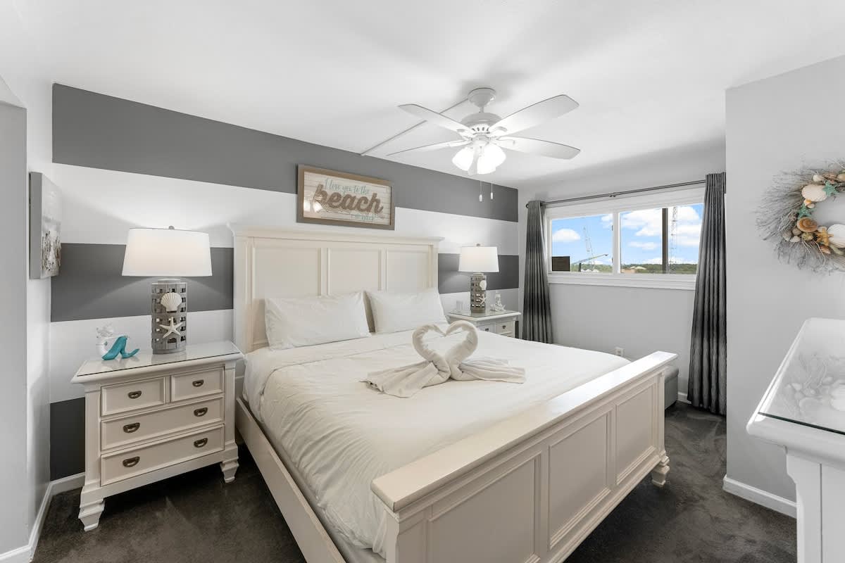 The Summit 1130 – Bedroom with a king-size bed, grey striped walls, nightstands, window view, and decorative items.