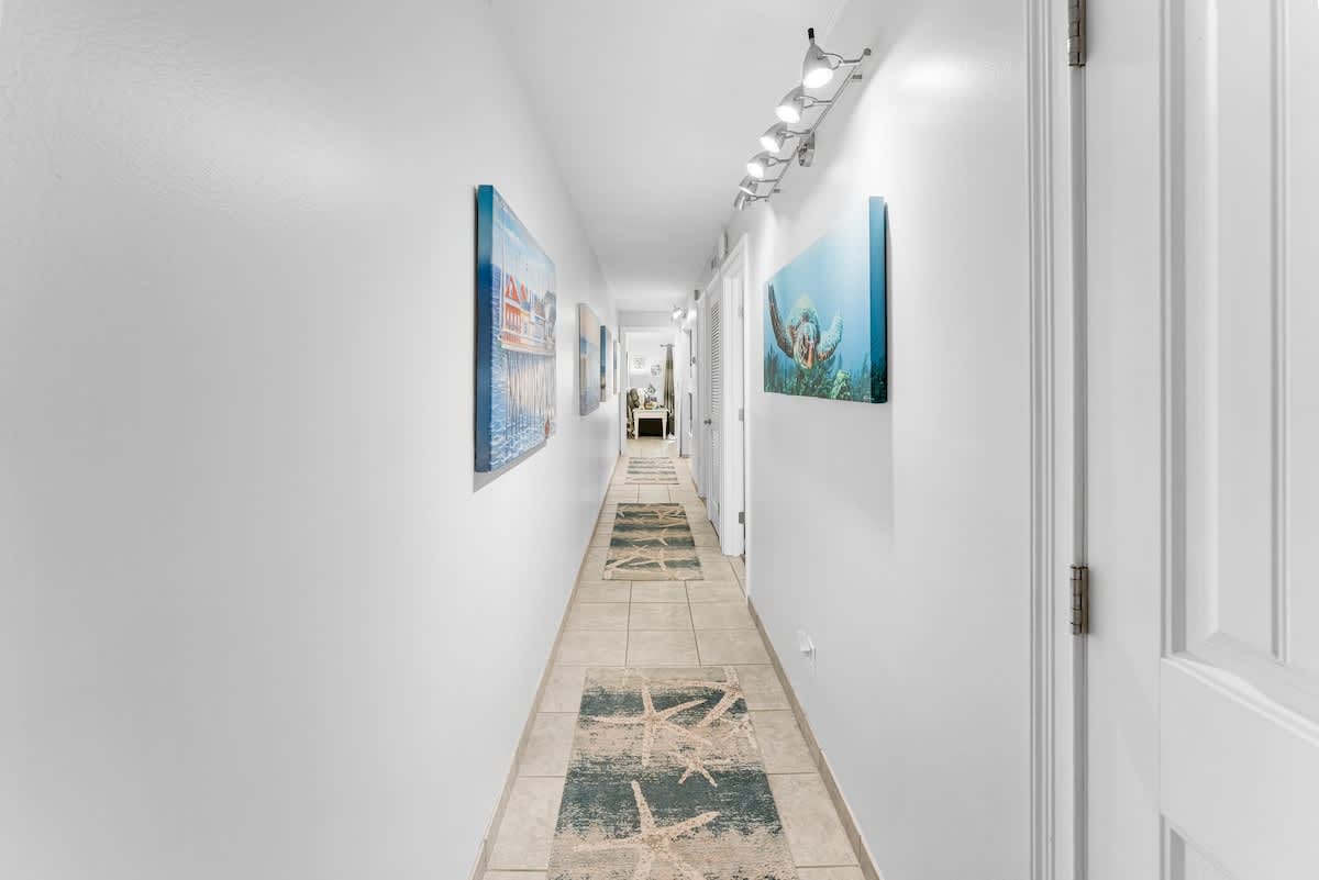 The Summit 1130 – Long hallway with tile flooring, artwork on the walls, and a carpet runner featuring starfish designs.
