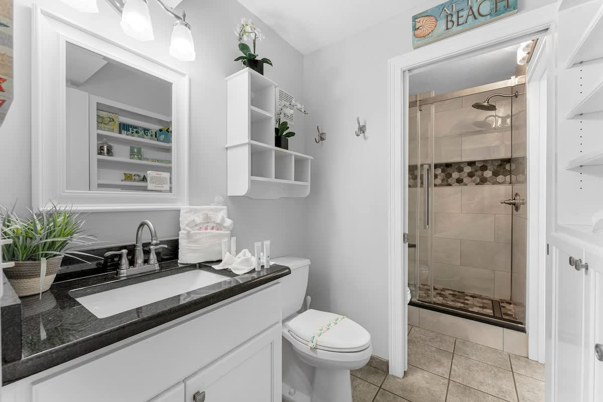 The Summit 1130 – Bathroom featuring a dark countertop, white cabinetry, shower stall, mirror, and decorative shelving.