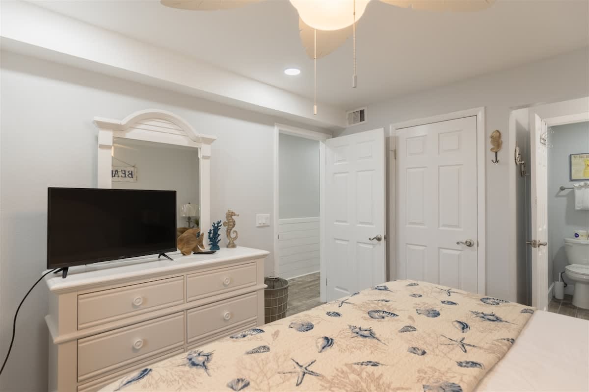 The Summit 504 – Bedroom with a dresser, television, seashell decor, and two doors leading to bathroom and hallway.