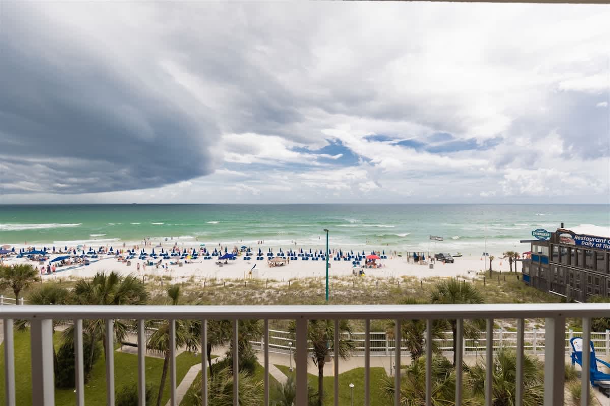 The Summit 504 – View of beach with lounge chairs, ocean, and cloudy sky from balcony of a rental unit.