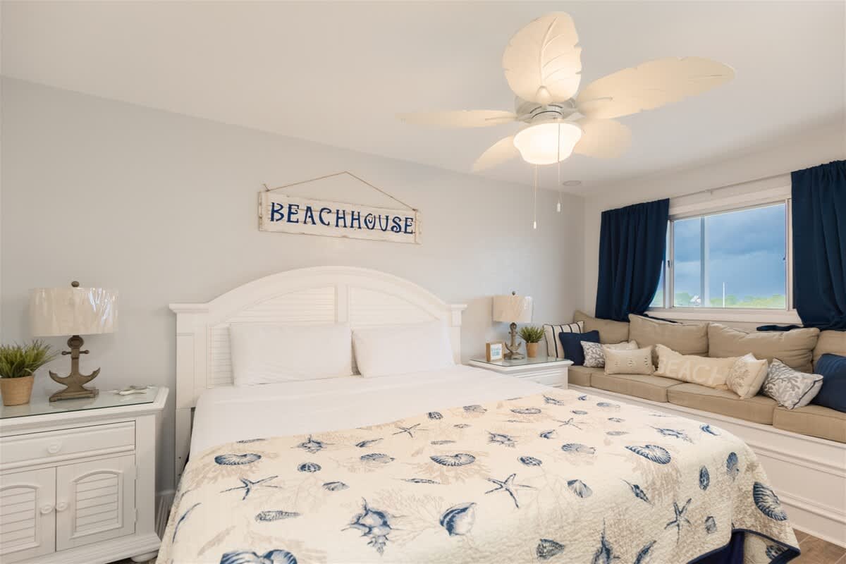The Summit 504 – Cozy bedroom with a large bed, beach-themed decor, window seat, and ceiling fan.