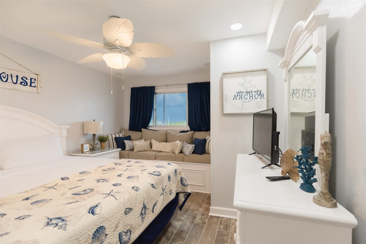 The Summit 504 – Cozy bedroom with a king bed, seating area, and blue curtains, decorative sea-themed accents, and a ceiling fan.