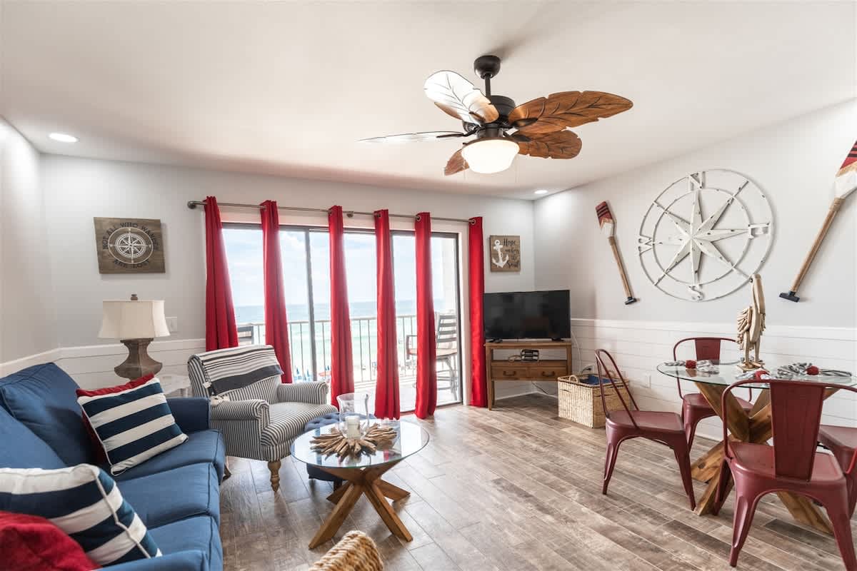 The Summit 504 – Cozy living area with red curtains, beach view, seating, TV, and dining table.
