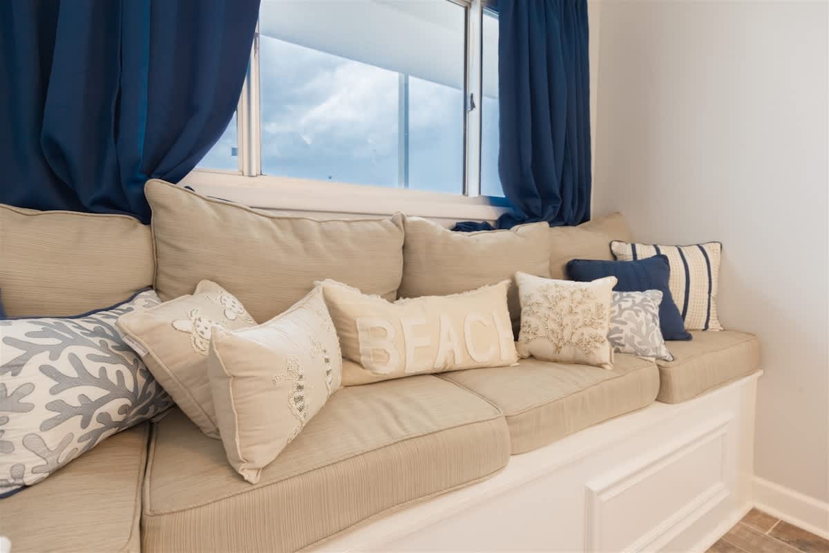 The Summit 504 – Cozy window seat with decorative pillows and blue curtains, overlooking a cloudy sky.