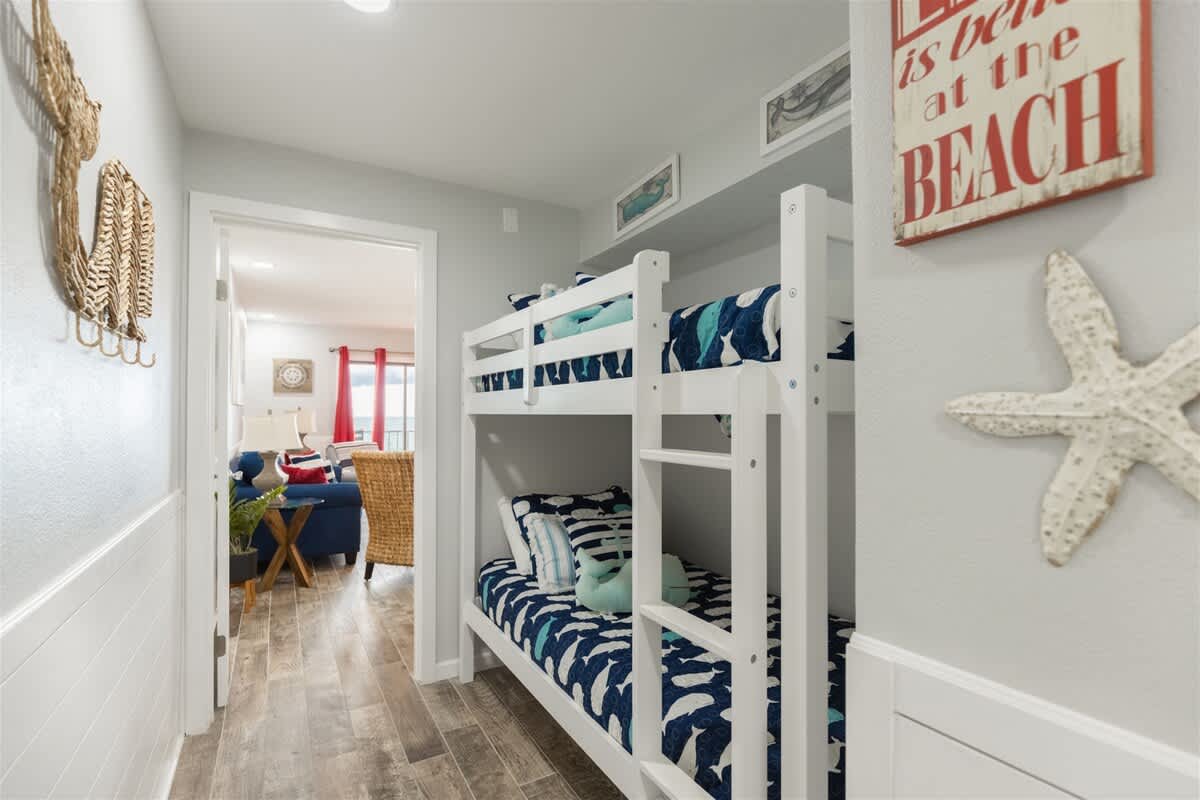 The Summit 504 – Bunk beds with playful bedding and a view into a living area with blue furniture and red curtains.
