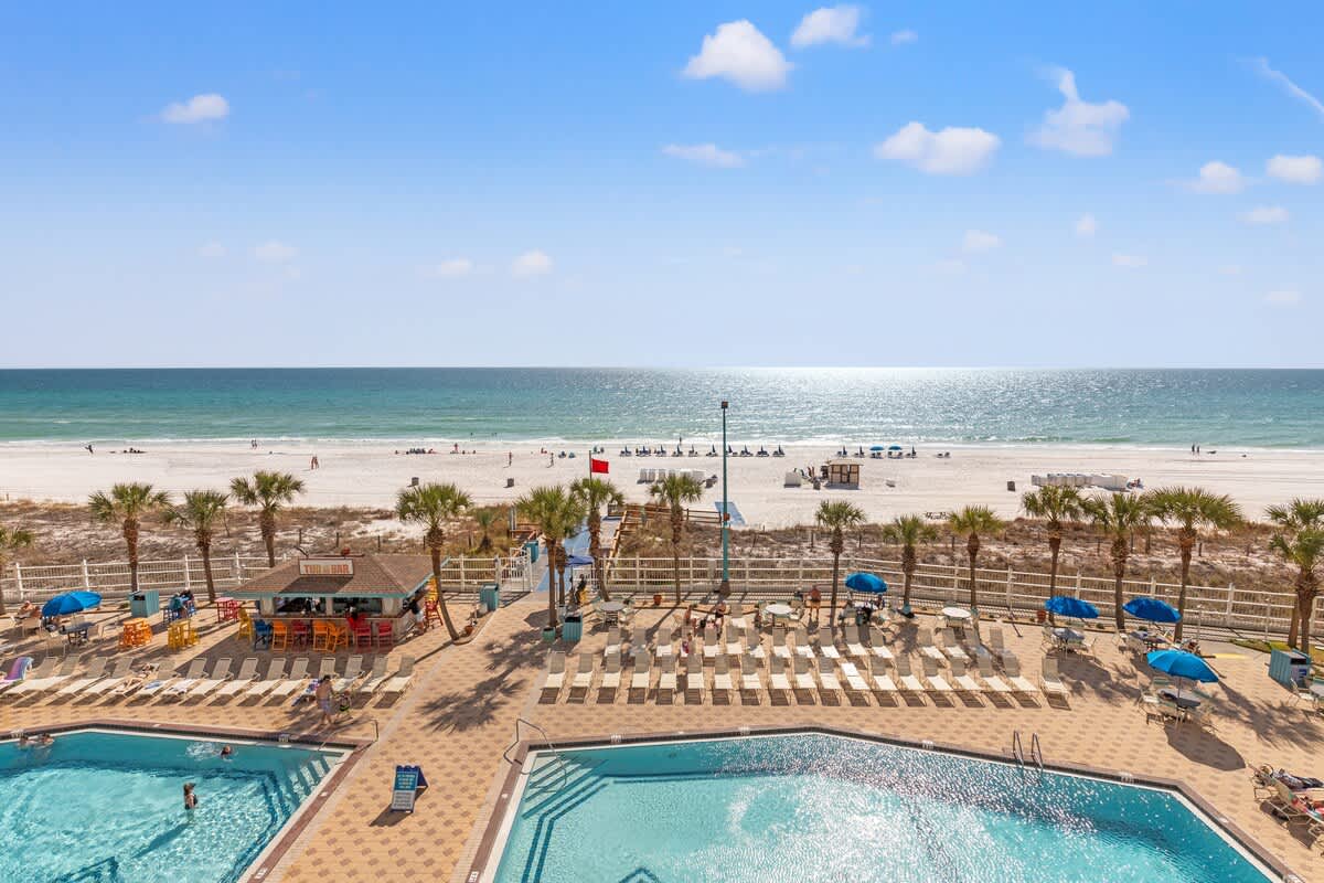 The Summit 515 – View of pools, beach, and ocean with umbrellas and palm trees in foreground.