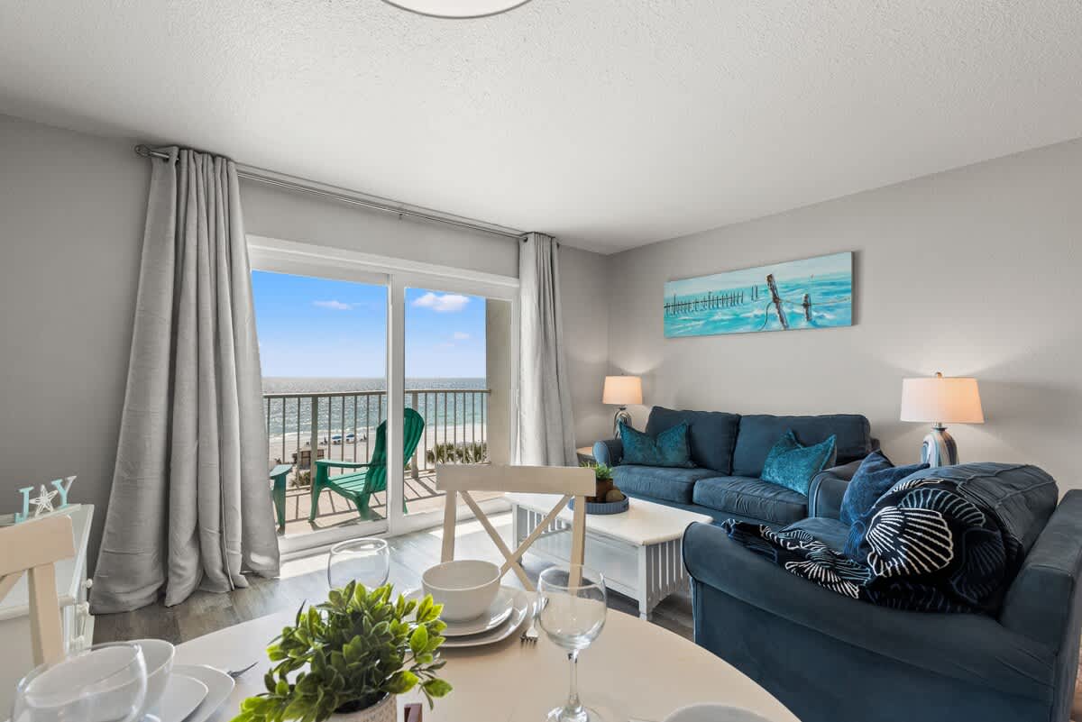 The Summit 515 – Cozy living area with blue sofas, dining table, and balcony view of the beach and ocean.
