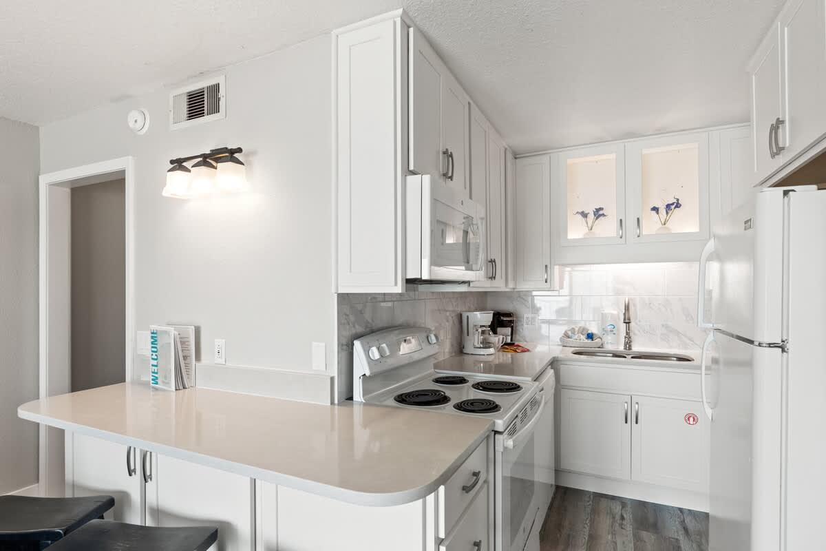 The Summit 515 – Compact white kitchen with modern appliances, bar seating, and gray walls.