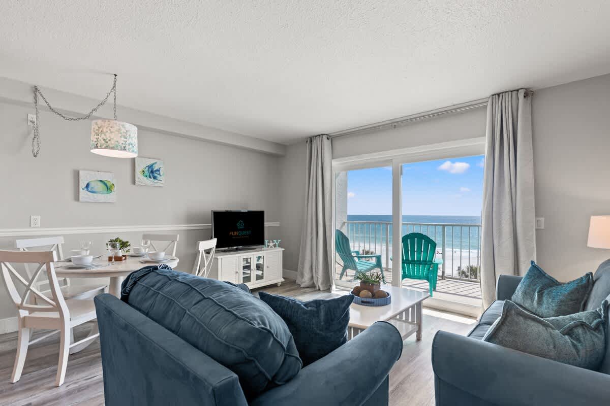 The Summit 515 – Cozy living room with ocean view, dining area, and teal patio chairs on the balcony.
