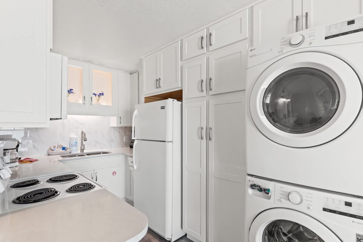 The Summit 515 – Bright kitchen with white cabinets, electric stove, refrigerator, and stacked washer-dryer unit.