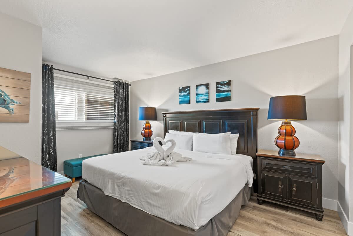 The Summit 515 – Cozy bedroom with a king-size bed, lamp, black curtains, and artwork on the walls.