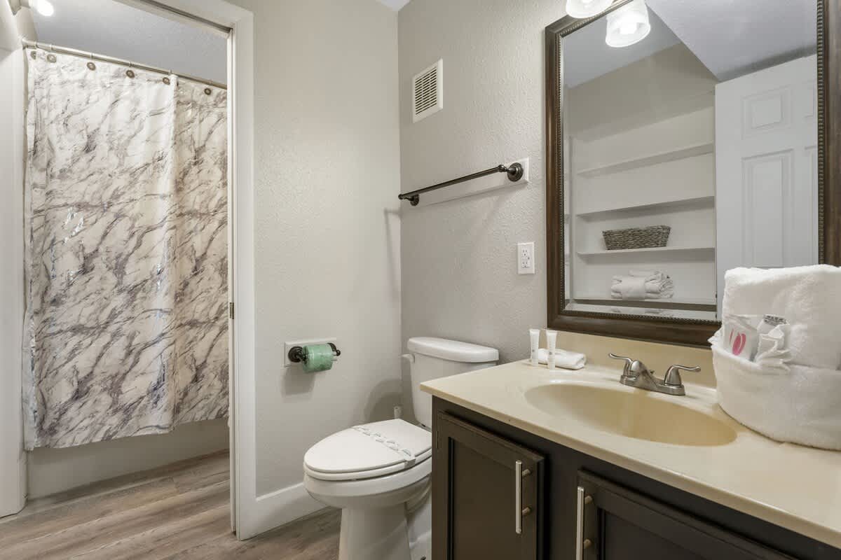 The Summit 515 – Bathroom with a marble-patterned shower curtain, sink, and toilet, featuring light wood flooring.