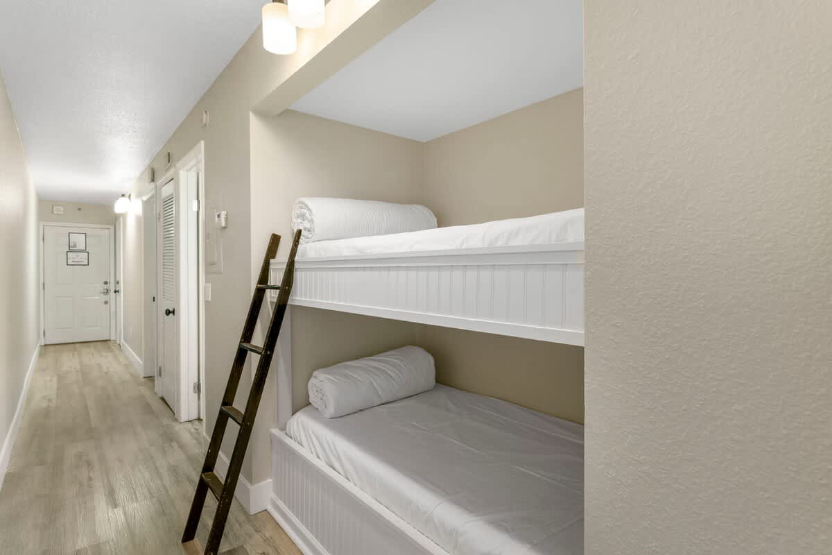 The Summit 515 – Bunk bed area with a wooden ladder, light-colored walls, and a door at the end of the hallway.