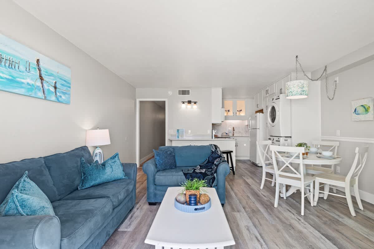 The Summit 515 – Living room with blue sofas, dining area, kitchen, and light-colored wood flooring.