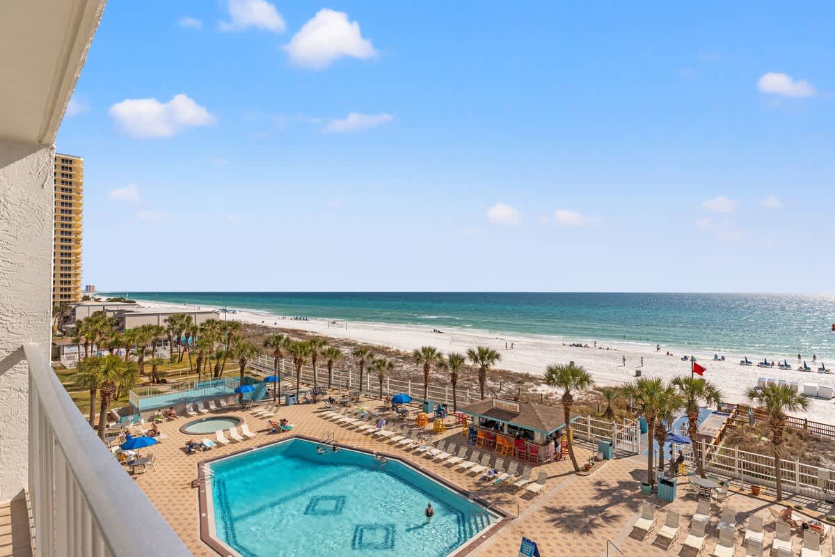 The Summit 515 – Ocean view from balcony overlooking a pool and beach with palm trees and loungers.