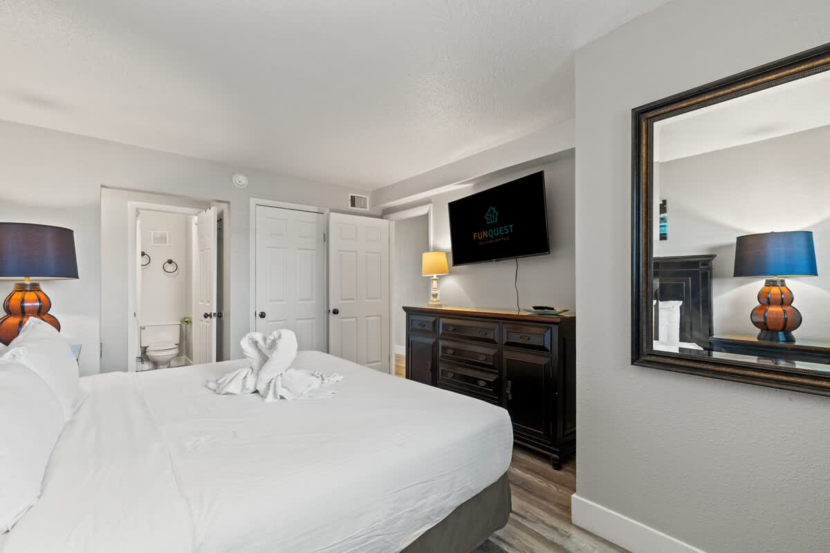 The Summit 515 – Cozy bedroom with a large bed, TV, dresser, lamp, and bathroom door visible.
