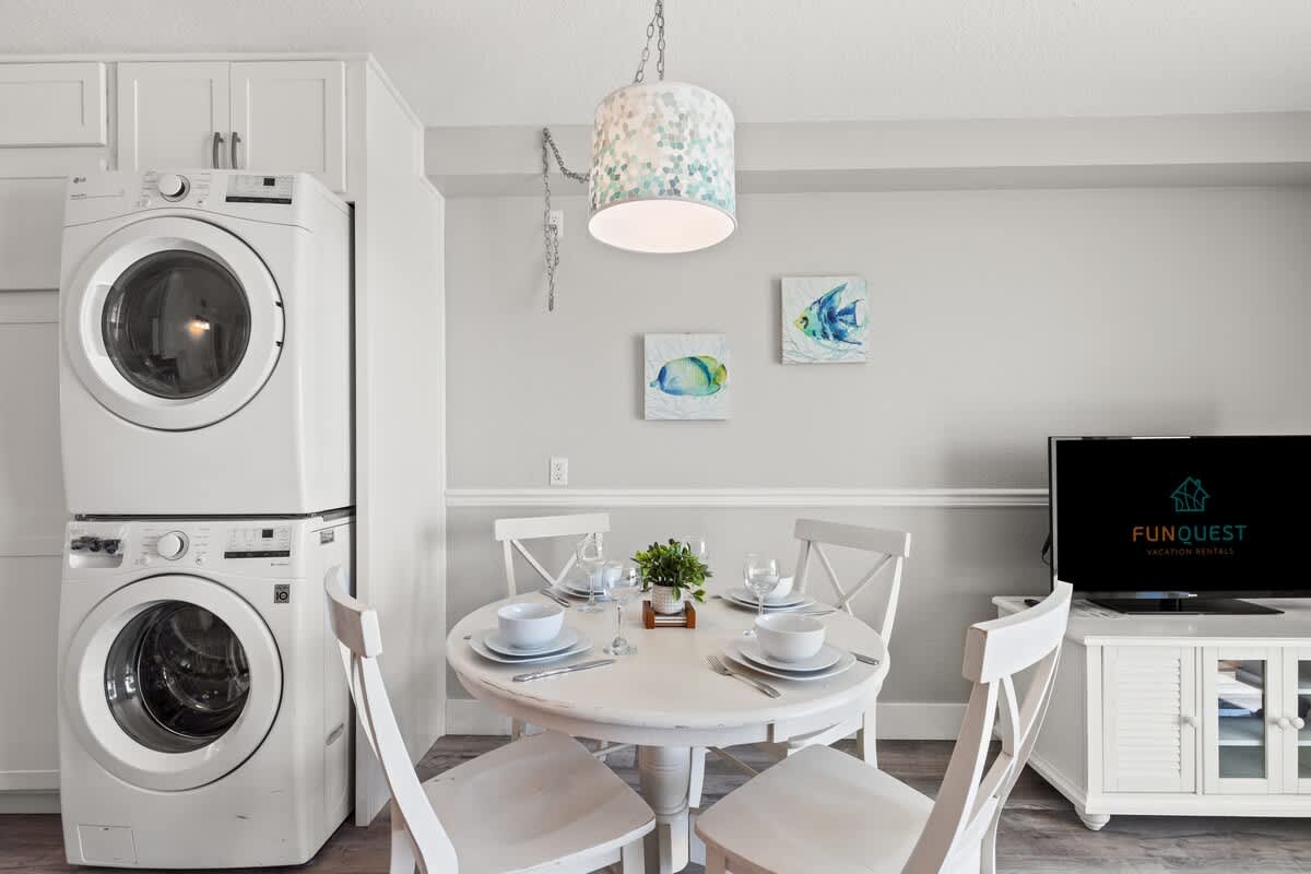 The Summit 515 – Dining area with a round table, four chairs, stacked washer and dryer, wall art, and television.