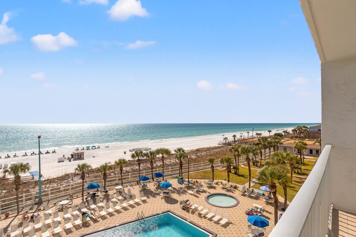 The Summit 515 – Ocean view from balcony with pool, palm trees, and beach chairs visible below.
