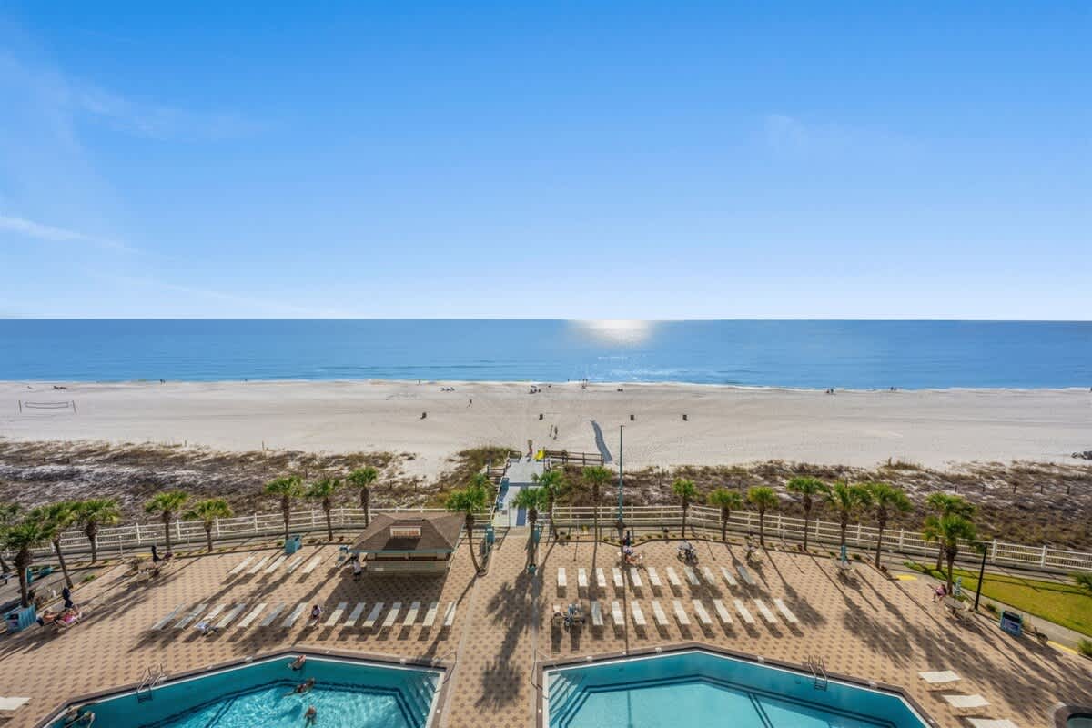 The Summit 816 – View of ocean, beach, and two swimming pools surrounded by palm trees at The Summit 816.