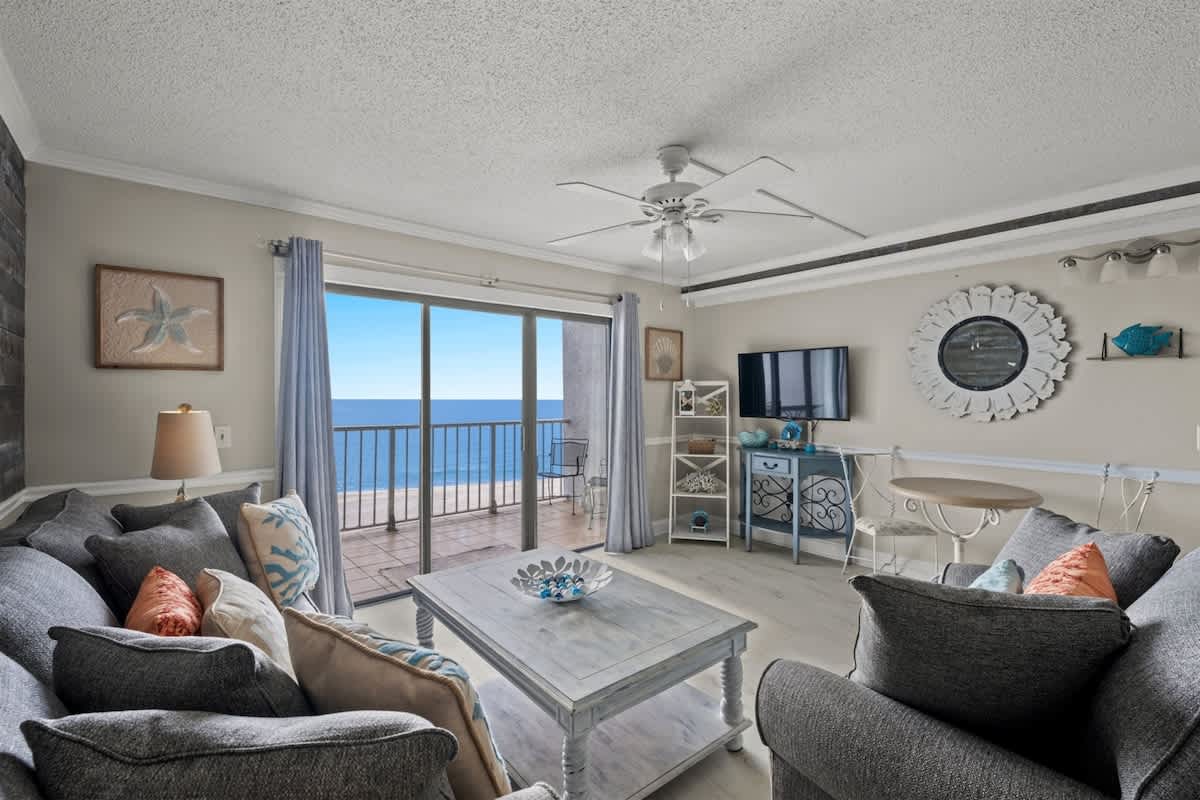 The Summit 816 – Living room with gray sofas, ocean view, sliding glass doors, and a small dining table.