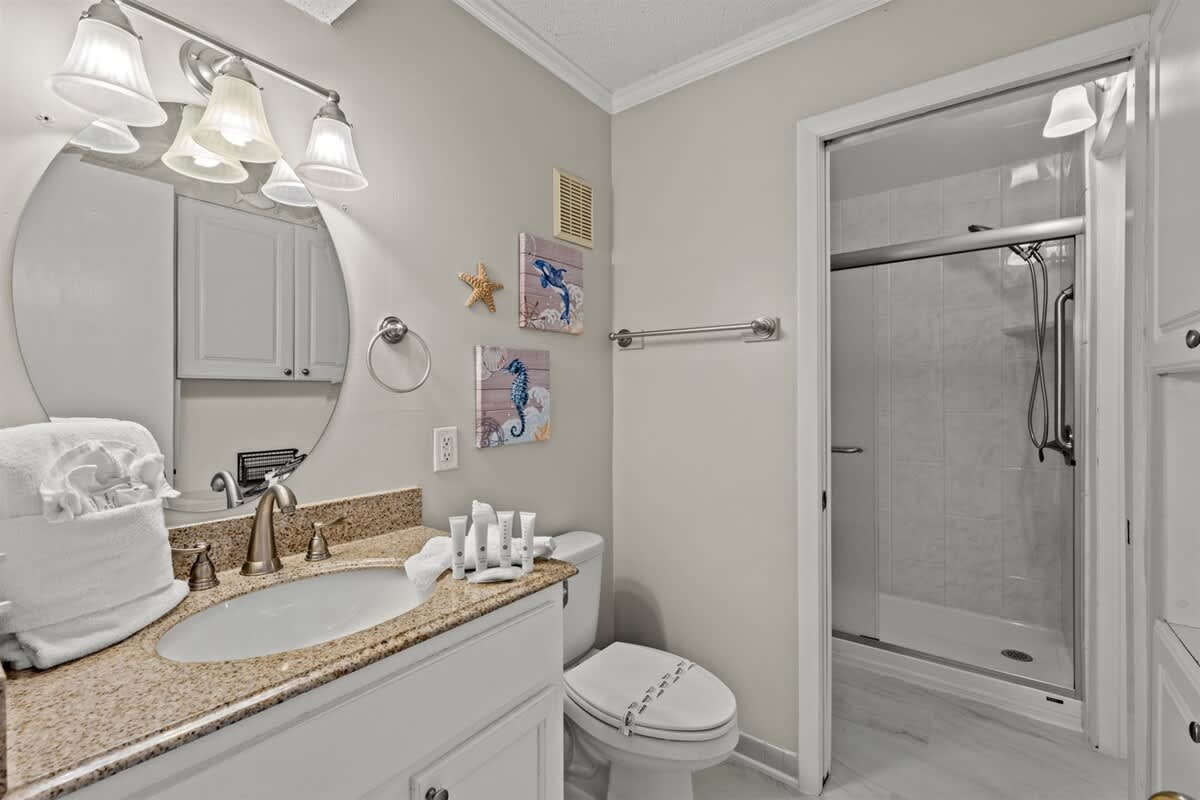 The Summit 816 – Bathroom with a circular mirror, granite countertop, shower, and decorative wall art.