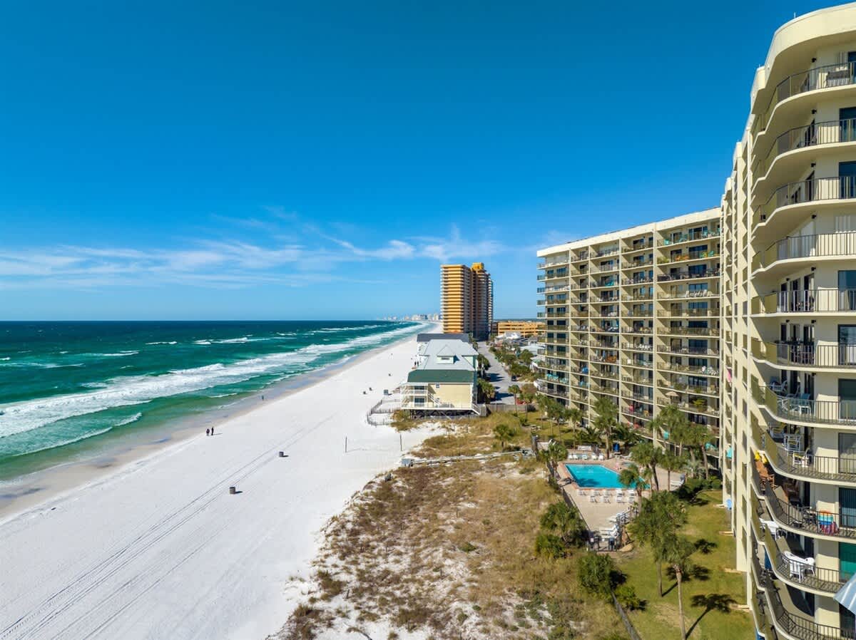 The Summit 816 – View of beach with white sand, ocean waves, and nearby vacation rental buildings, including pool area.