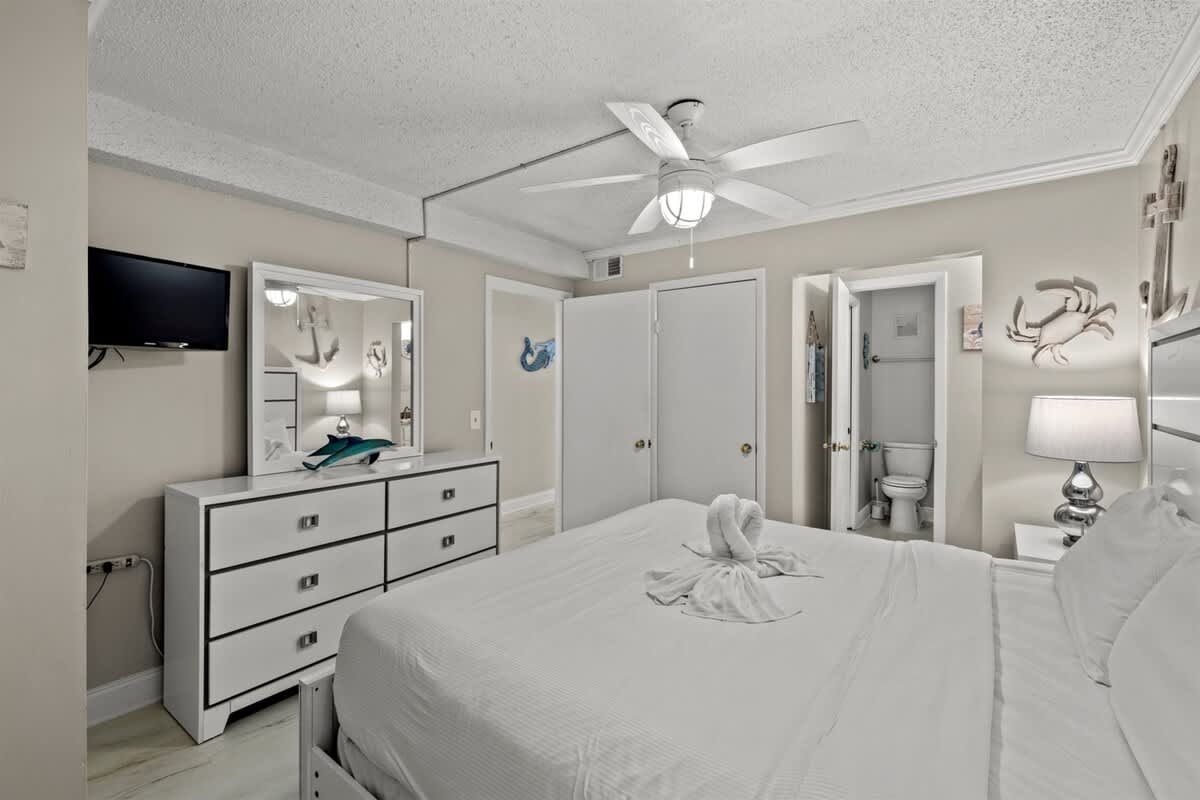 The Summit 816 – Bedroom with a queen bed, dresser, TV, and an ensuite bathroom door.