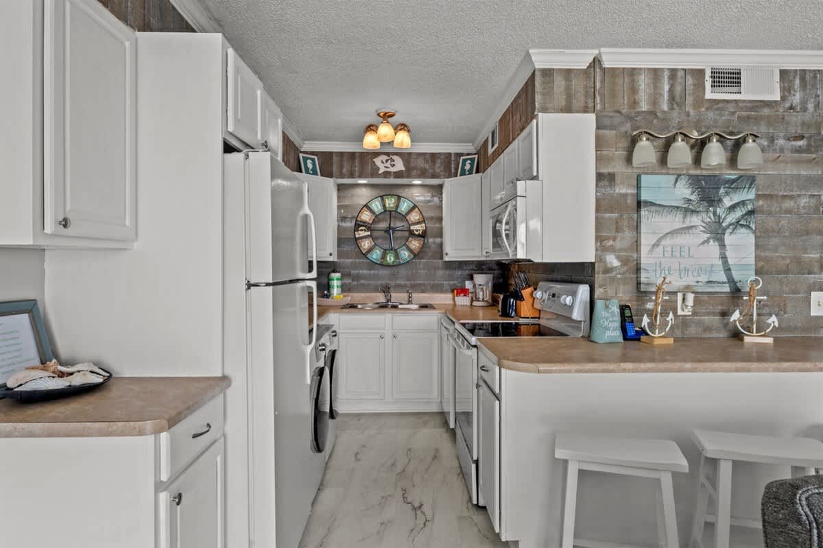 The Summit 816 – Bright kitchen with white cabinets, stainless steel appliances, and wooden accents featuring a decorative wall clock.