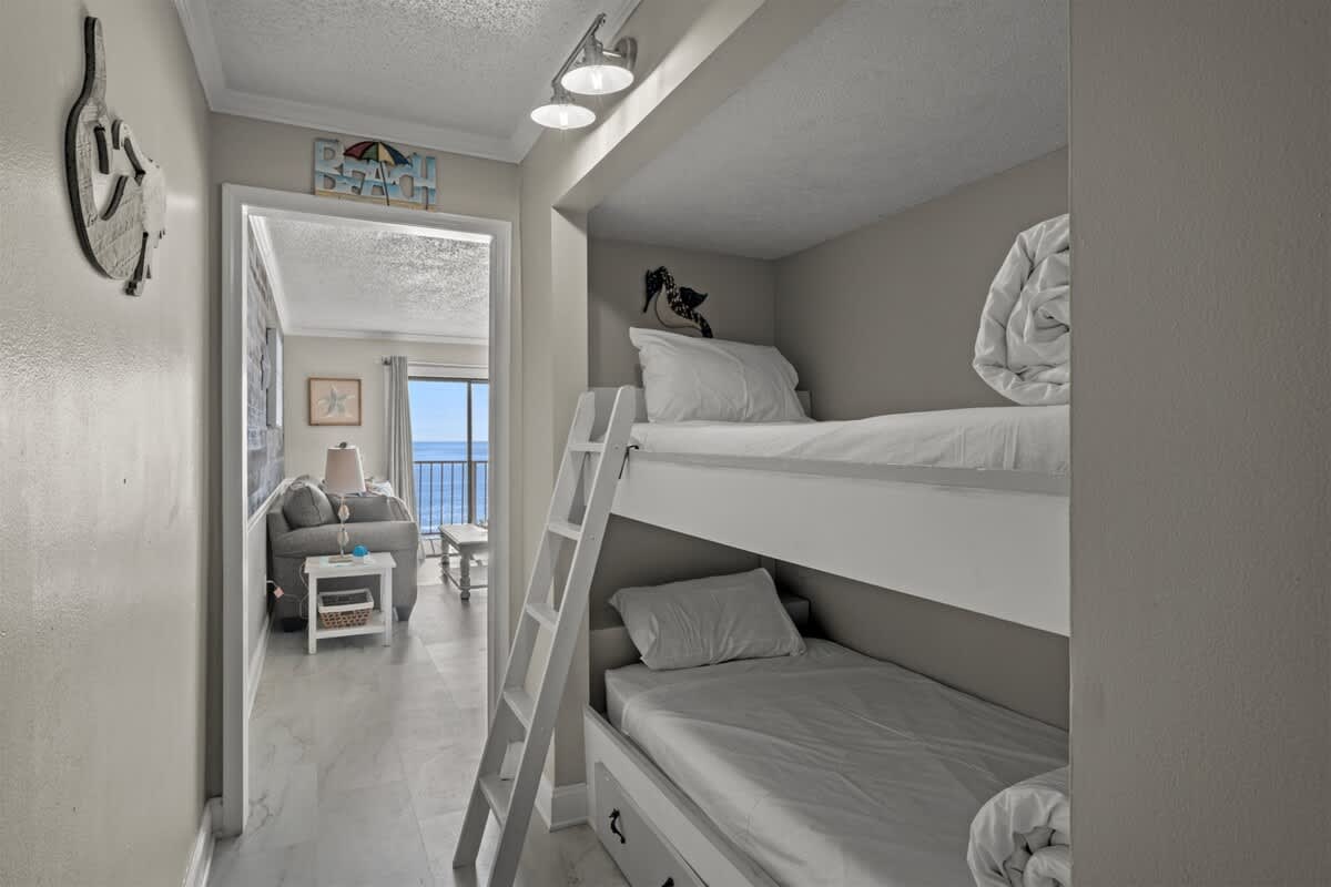The Summit 816 – Bunk beds in hallway with a view of a living room and ocean through large windows.