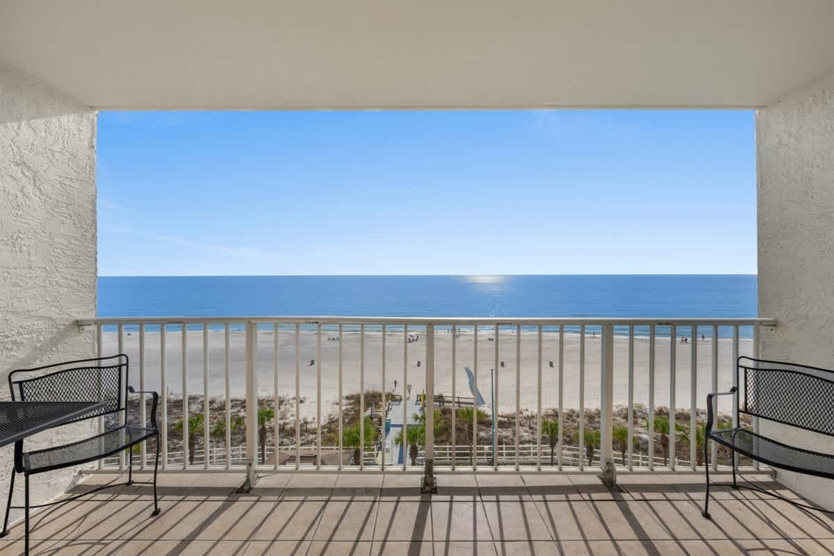 The Summit 816 – Ocean view from a balcony with two black chairs and sandy beach below.