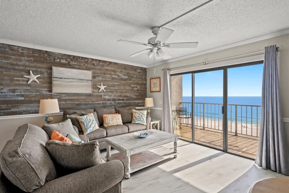 The Summit 816 – Living room with gray sofas, coastal decor, and ocean view through sliding glass doors.