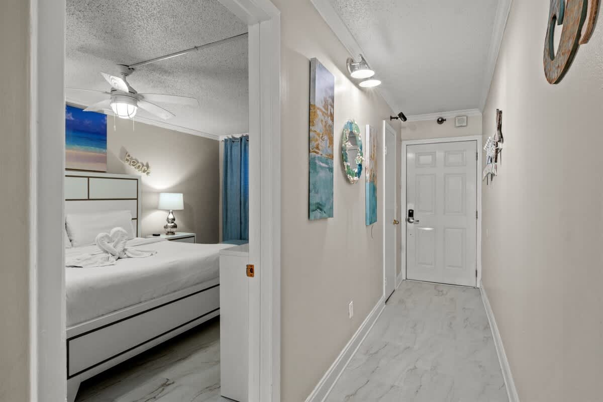 The Summit 816 – View of a hallway leading to a brightly lit bedroom with a king bed and decorative art.