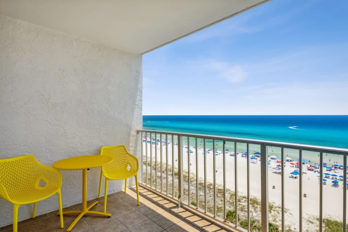 The Summit 1017 – Balcony with yellow chairs and table overlooking a beach and turquoise ocean.