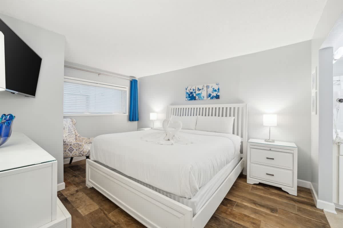 The Summit 1017 – Bright bedroom with a queen bed, TV, chair, white furniture, and window with blue curtains.