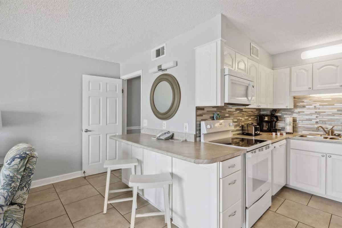 The Summit 1017 – Modern kitchen with white cabinets, tiled backsplash, microwave, and bar seating in a vacation rental.