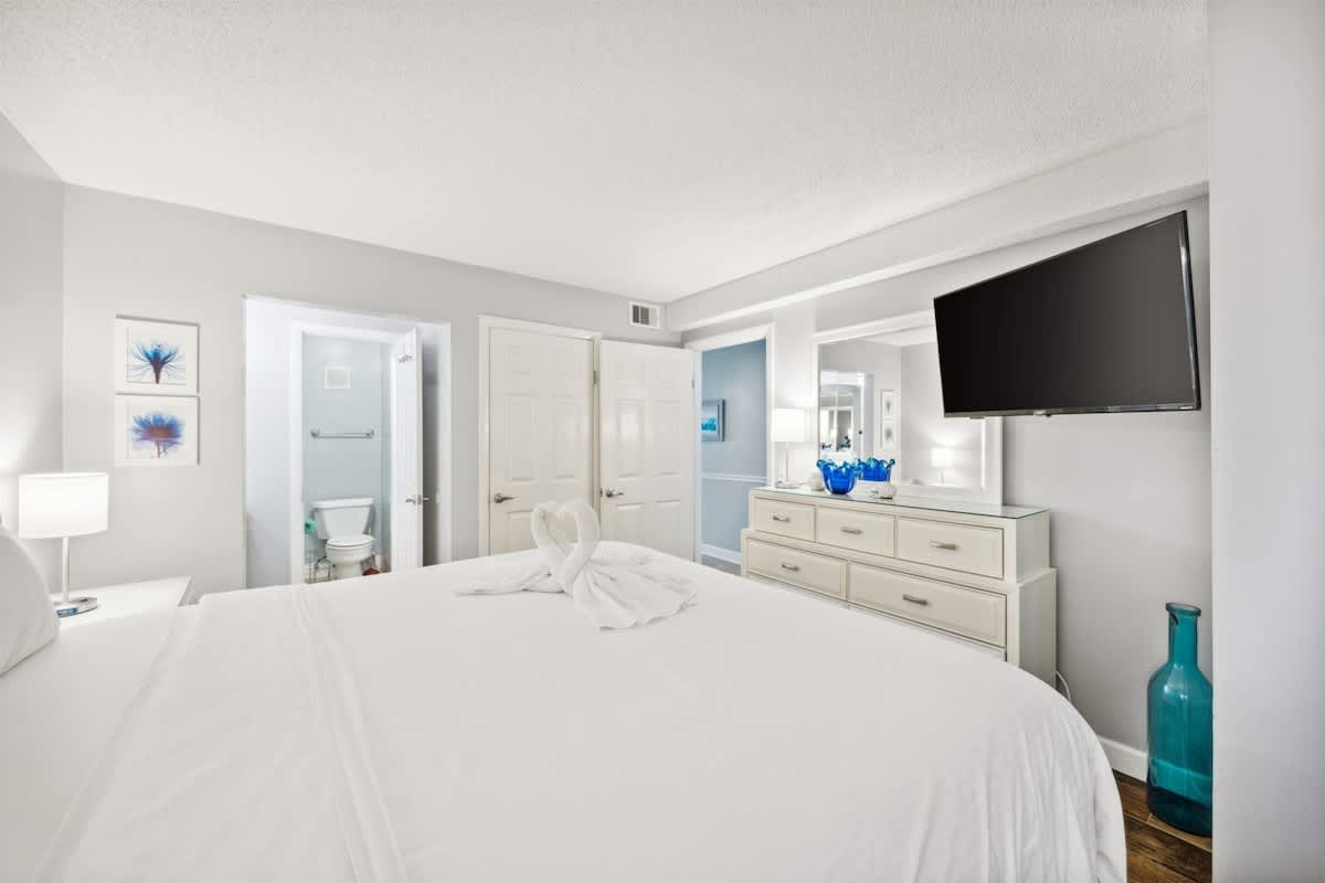 The Summit 1017 – Bedroom with a king bed, dresser, TV, and bathroom door visible.