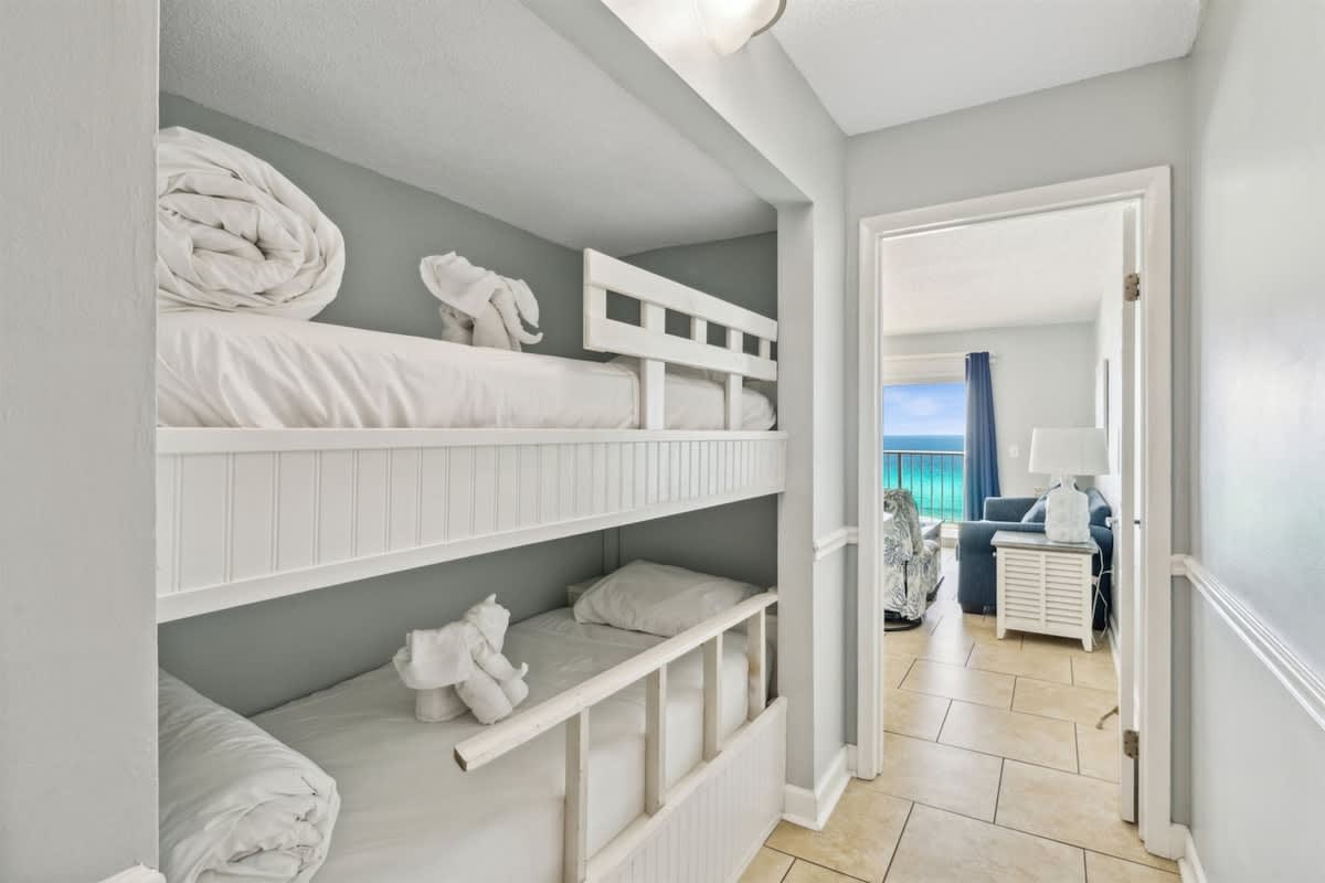 The Summit 1017 – Bunk beds in a small hallway with a view of the ocean through an open door.
