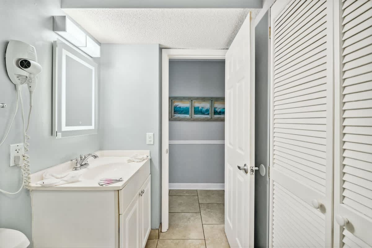 The Summit 1017 – Bathroom with a sink, mirror, closet door, and wall art in muted colors.