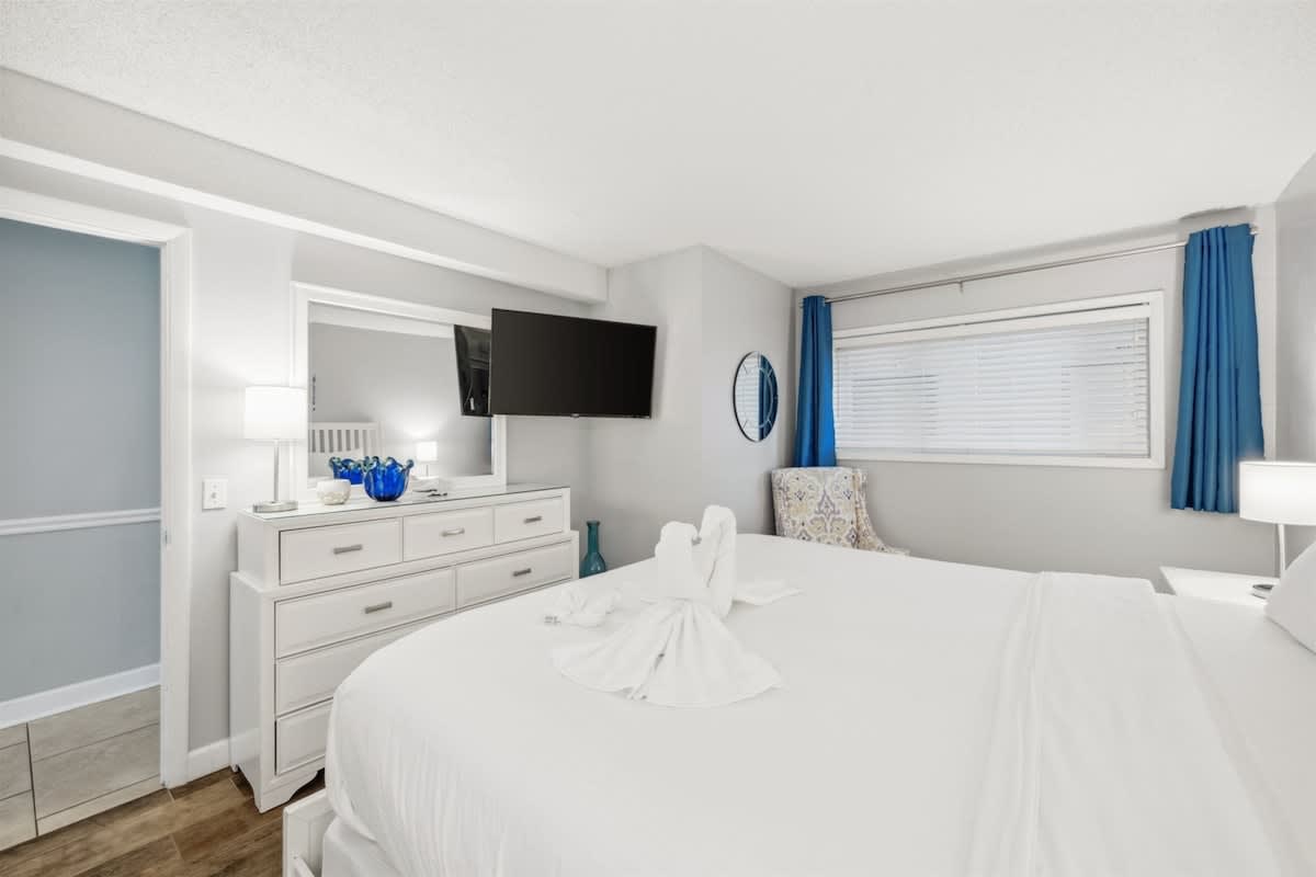 The Summit 1017 – Bright bedroom with a king bed, dresser, TV, and stylish chair by the window.