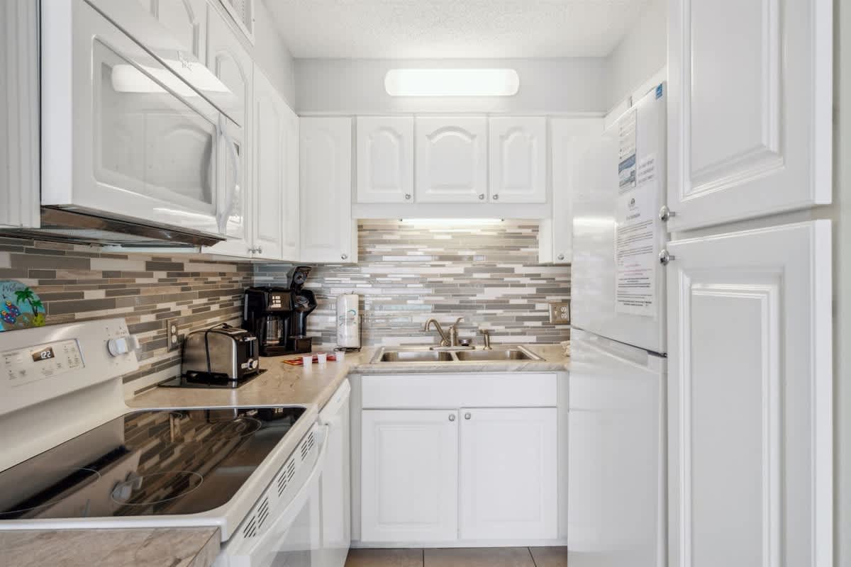 The Summit 1017 – Modern kitchen with white cabinets, stainless steel appliances, and tiled backsplash.