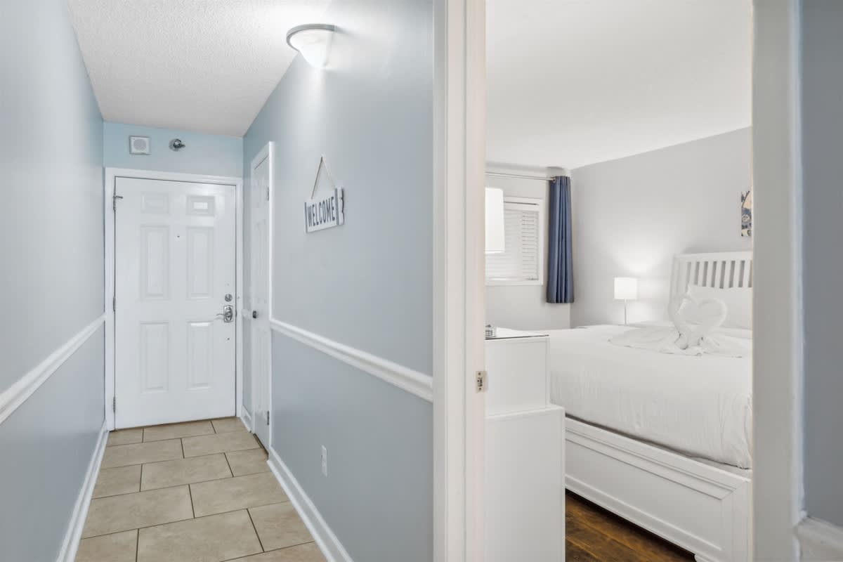 The Summit 1017 – Hallway leading to a bedroom with a white bed, nightstand, and decorative towels arranged.