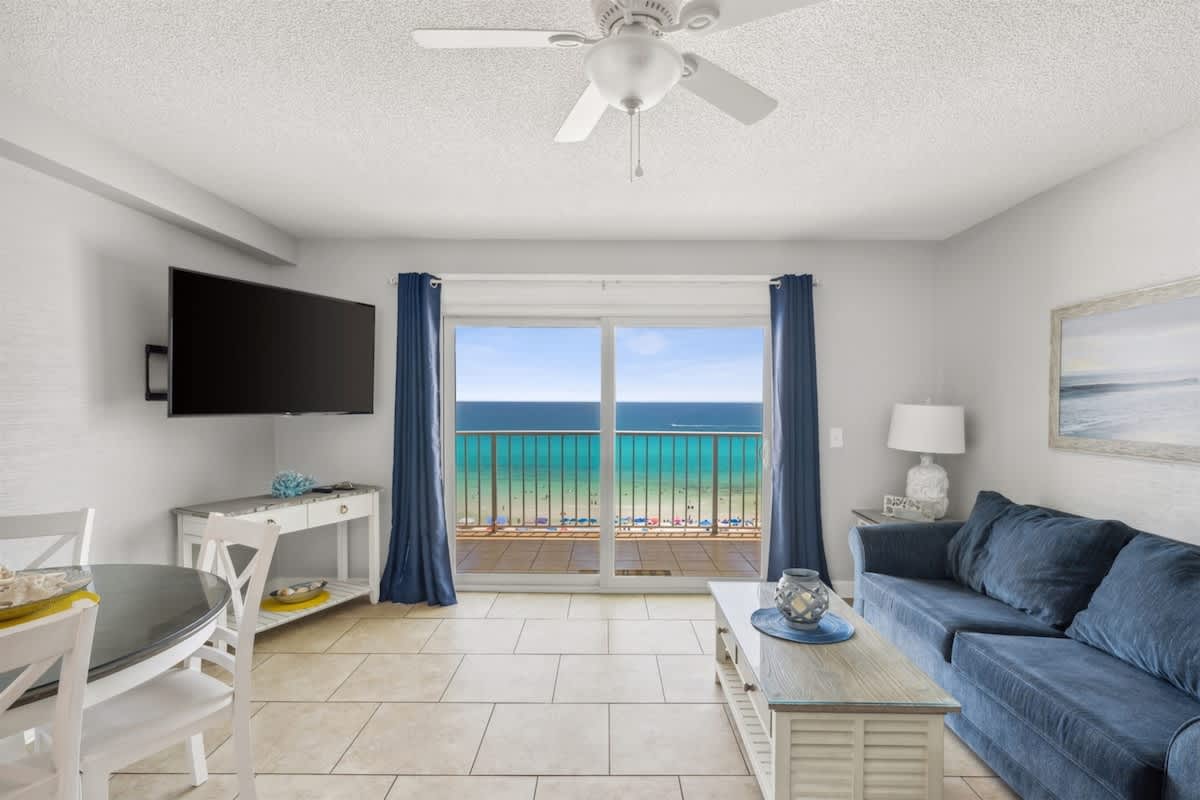 The Summit 1017 – Living room with ocean view, blue sofa, dining table, and flat-screen TV.