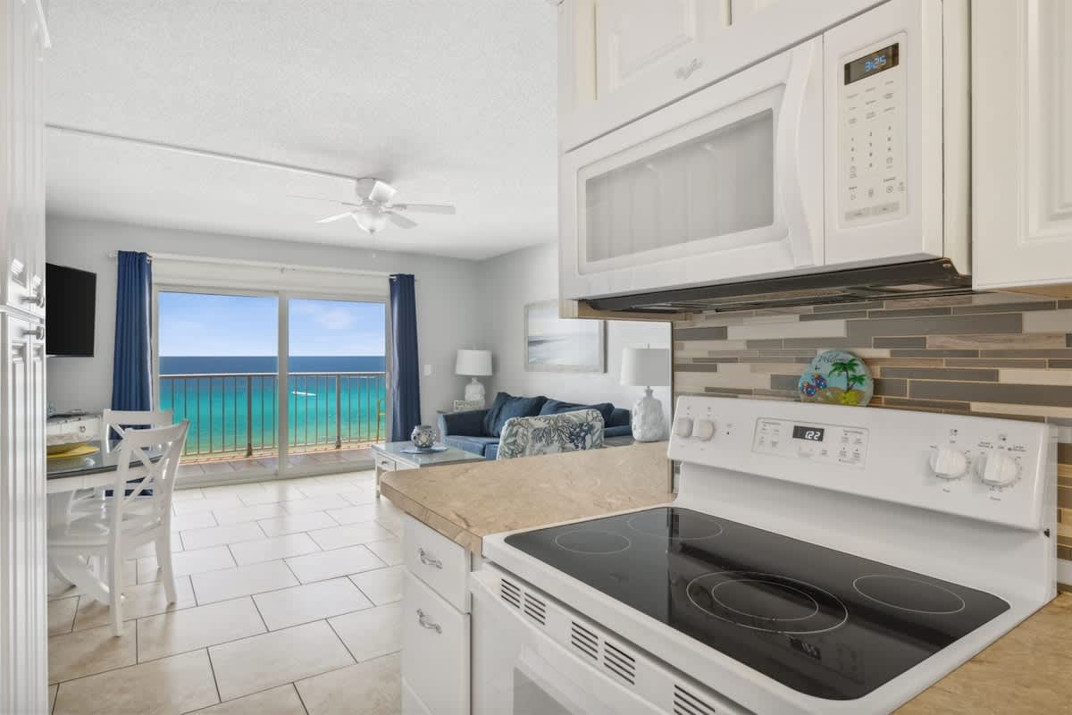 The Summit 1017 – Cozy kitchen with white appliances, dining area, and ocean view through large sliding glass doors.