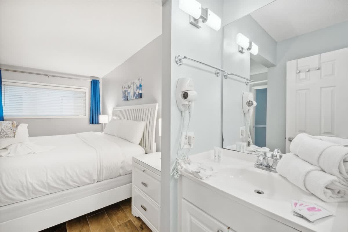 The Summit 1017 – Cozy bedroom with a white bed, blue curtains, and adjacent bathroom with a sink and towels.
