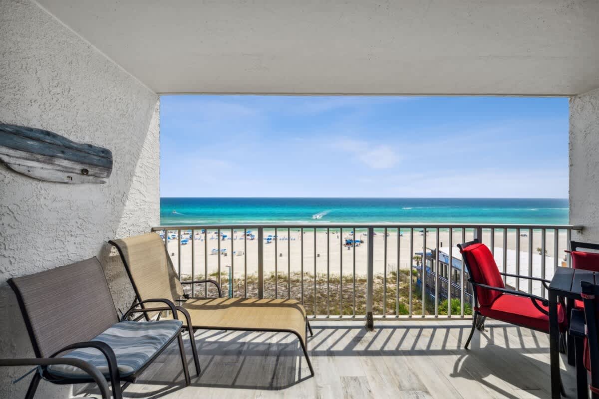 The Summit 702 – Balcony view of beach, ocean, and two outdoor chairs with red and beige accents.