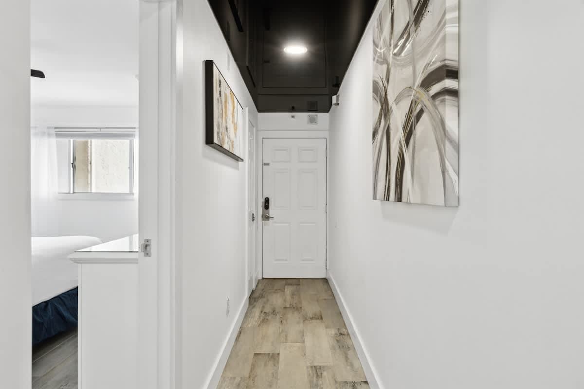 The Summit 702 – Interior hallway with white walls, wooden flooring, artwork, and a door at the end.