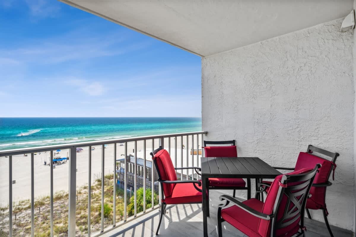The Summit 702 – Balcony with red chairs and table overlooking the beach and ocean.