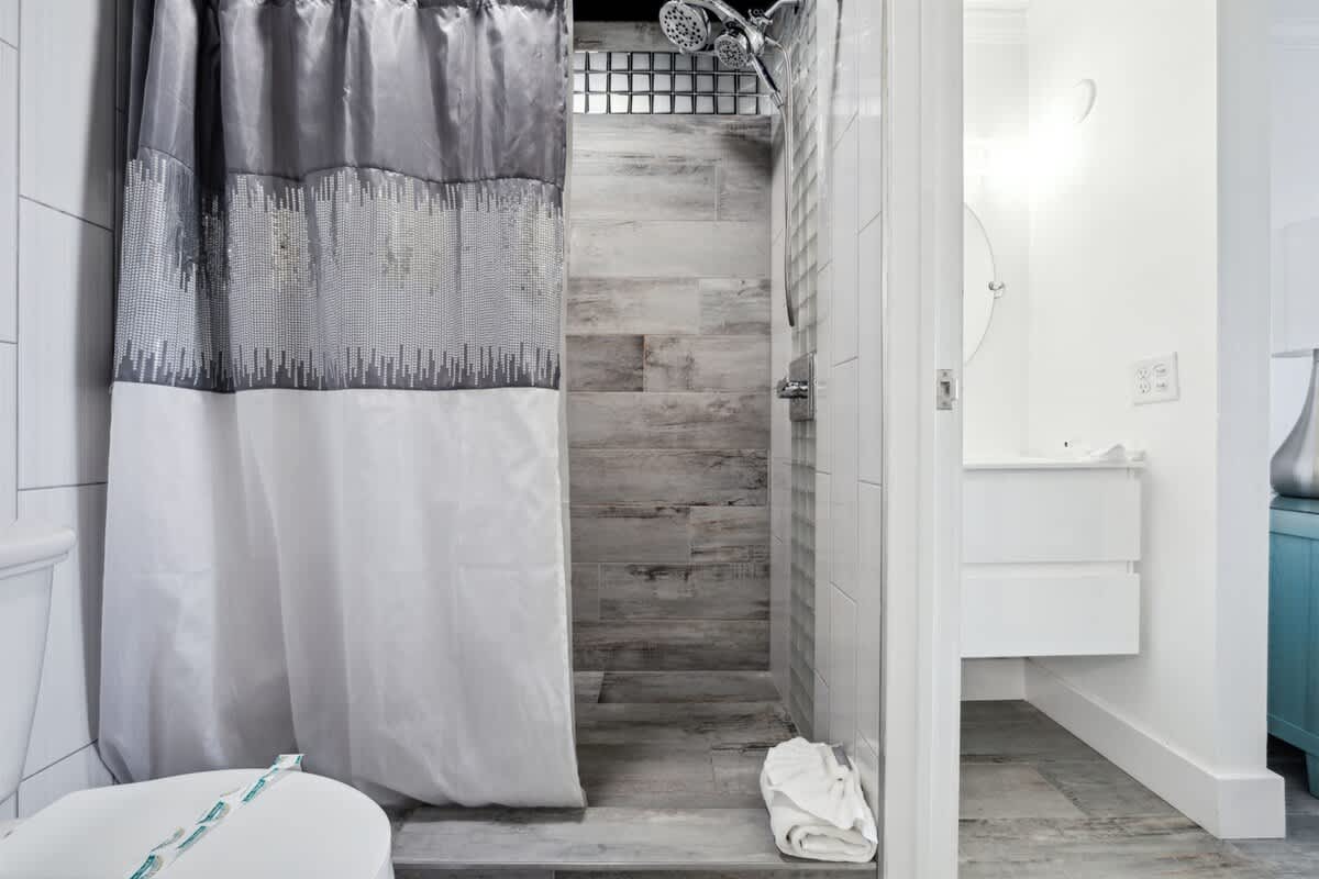 The Summit 702 – Modern bathroom with a walk-in shower, gray and white shower curtain, and light tile flooring.
